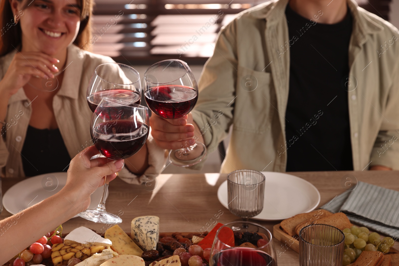 Photo of People clinking glasses of red wine at served table, closeup