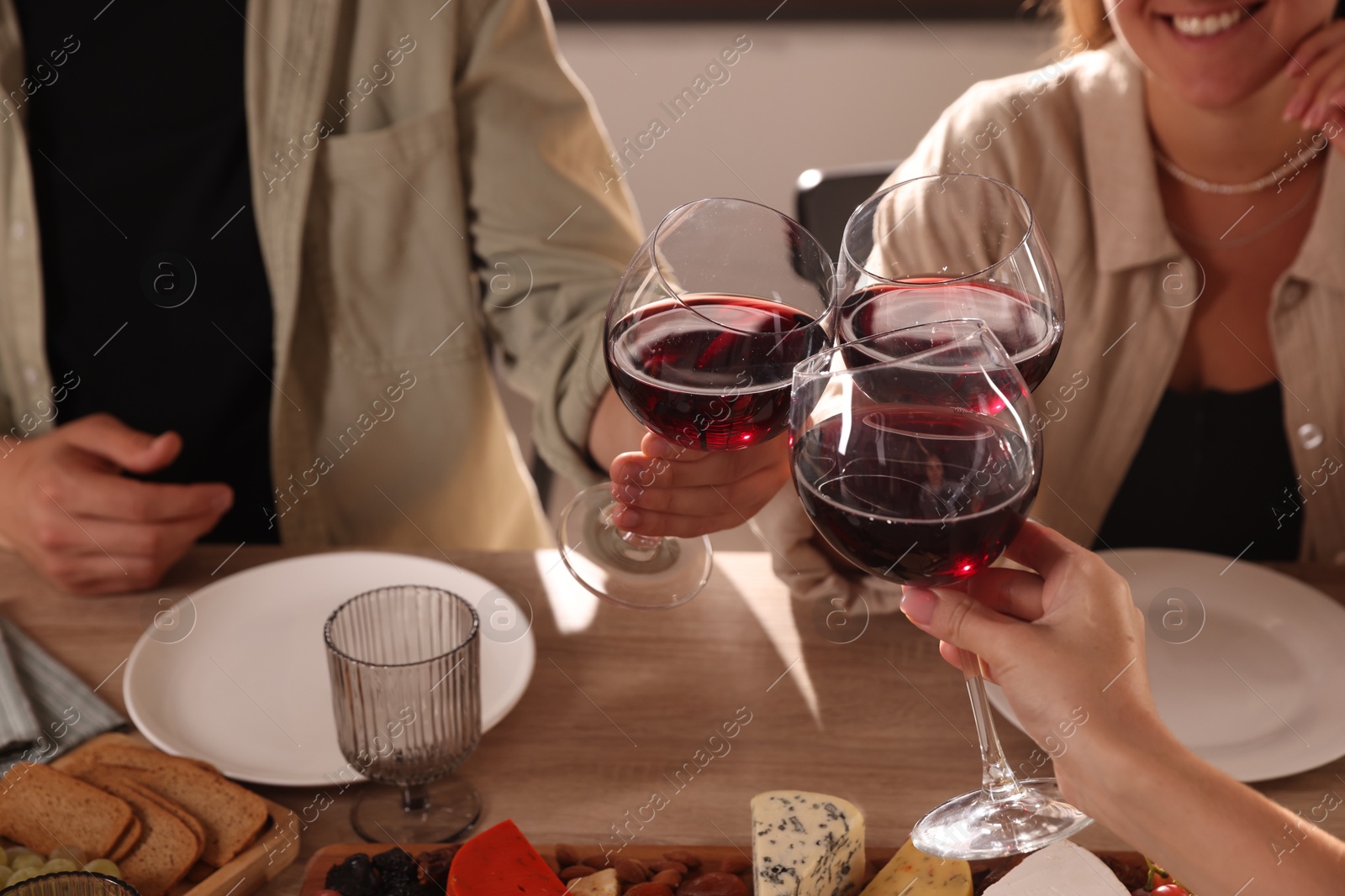 Photo of People clinking glasses of red wine at served table, closeup