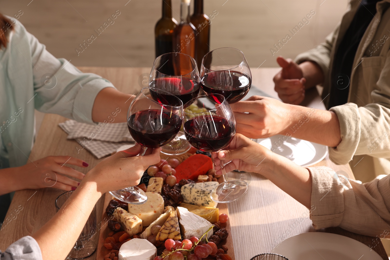 Photo of People clinking glasses of red wine at served table, closeup