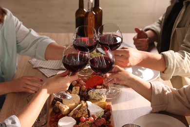 Photo of People clinking glasses of red wine at served table, closeup