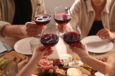 People clinking glasses of red wine at served table, closeup