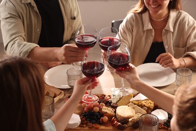 Photo of People clinking glasses of red wine at served table, closeup