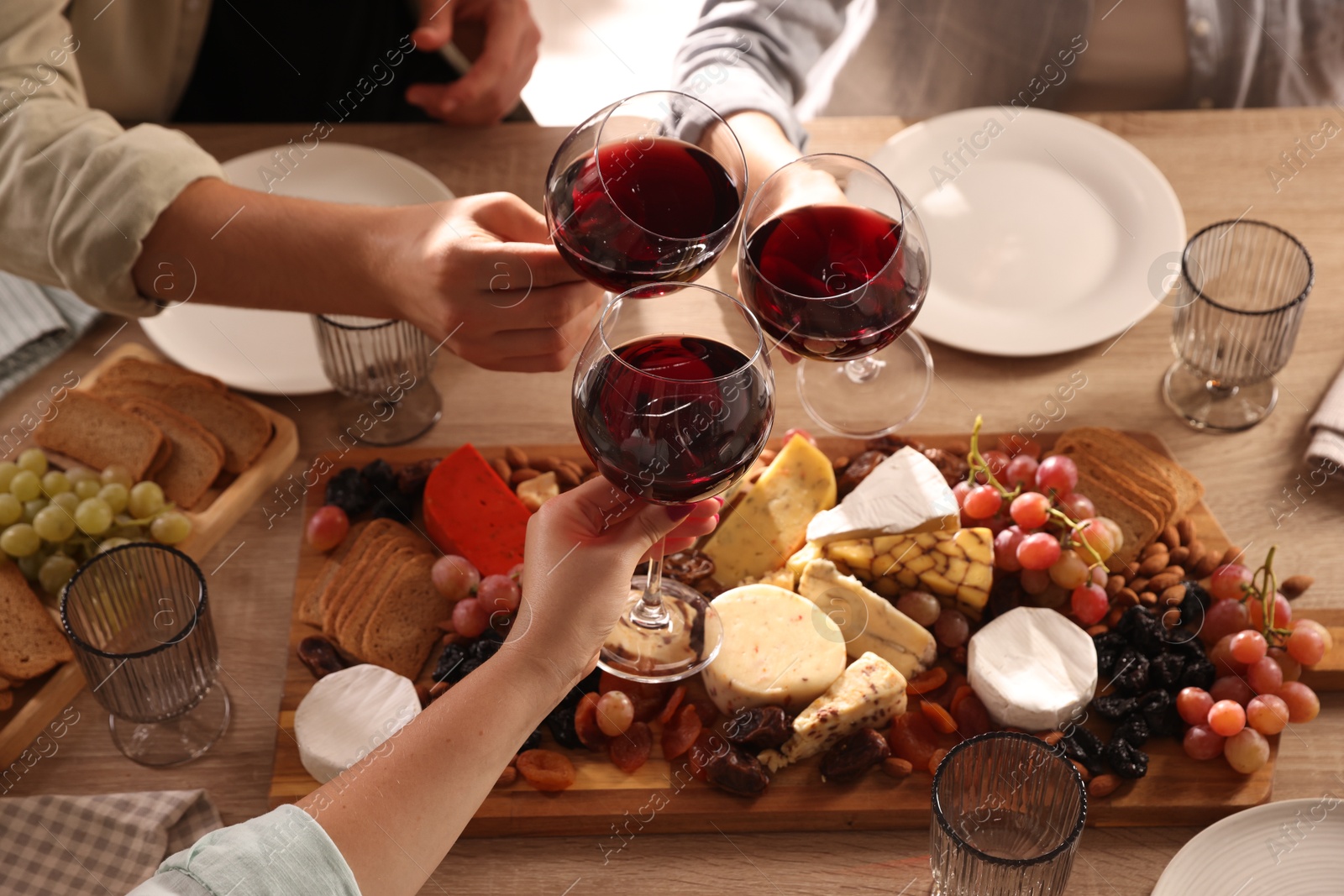 Photo of People clinking glasses of red wine at served table, closeup