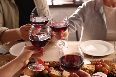 Photo of People clinking glasses of red wine at served table, closeup