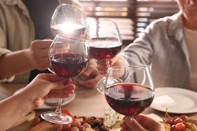 Photo of People clinking glasses of red wine at served table, closeup