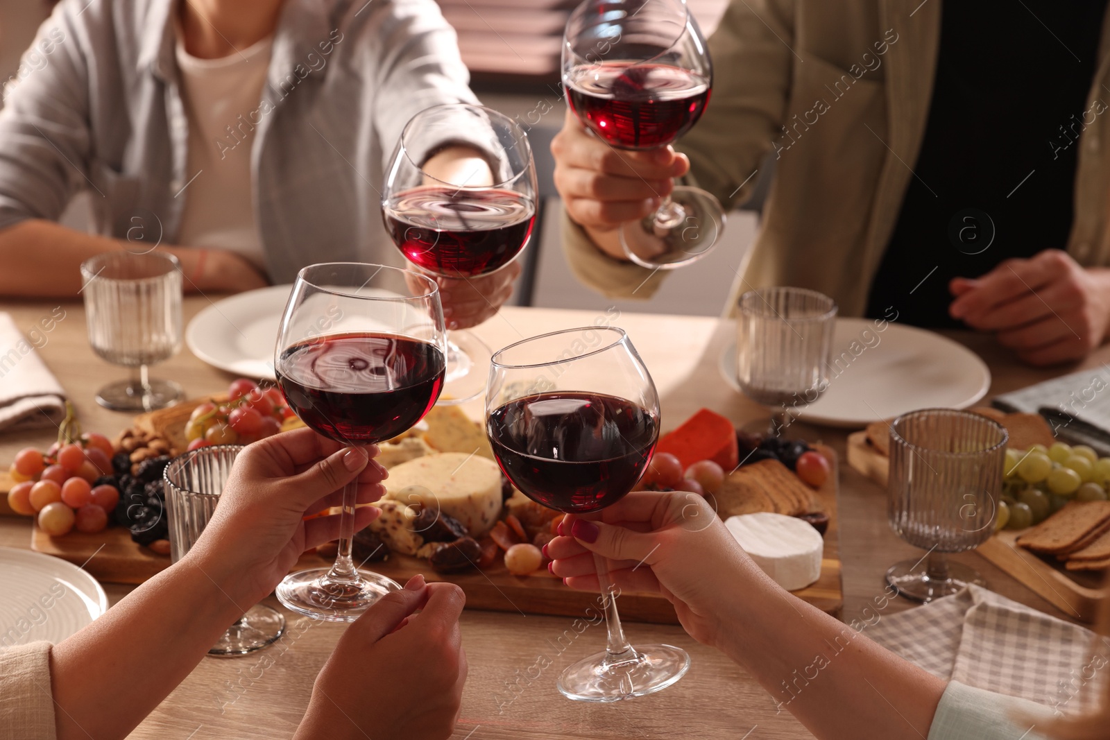 Photo of People clinking glasses of red wine at served table, closeup