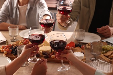 People clinking glasses of red wine at served table, closeup