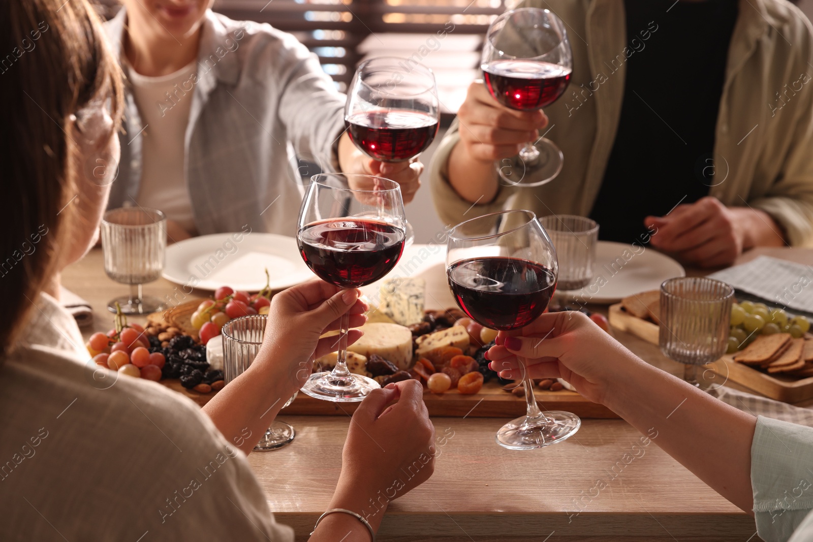 Photo of People clinking glasses of red wine at served table, closeup