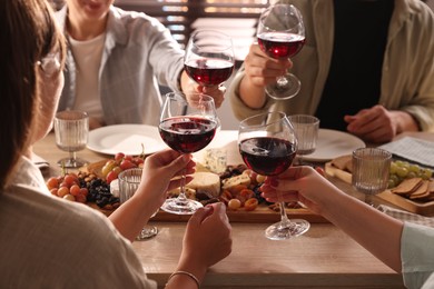 People clinking glasses of red wine at served table, closeup