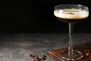 Glass of delicious espresso martini and coffee beans on dark textured table, closeup. Space for text