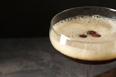 Delicious espresso martini with coffee beans in glass on blurred background, closeup. Space for text