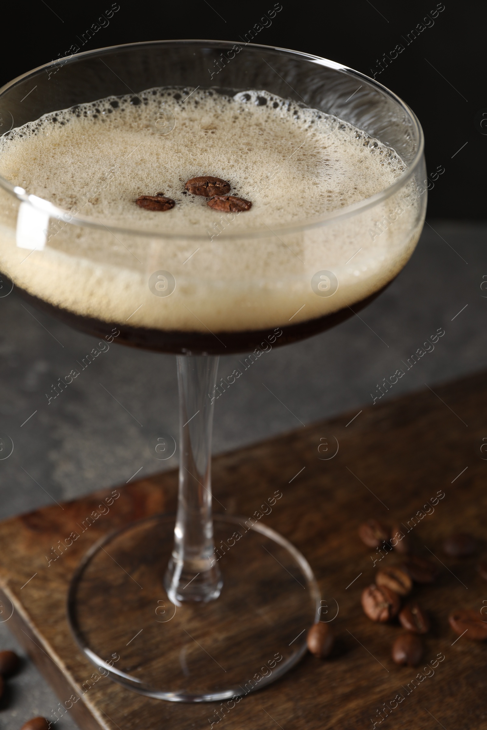 Photo of Glass of delicious espresso martini and coffee beans on dark textured table, closeup