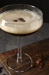 Photo of Glass of delicious espresso martini and coffee beans on dark textured table, closeup