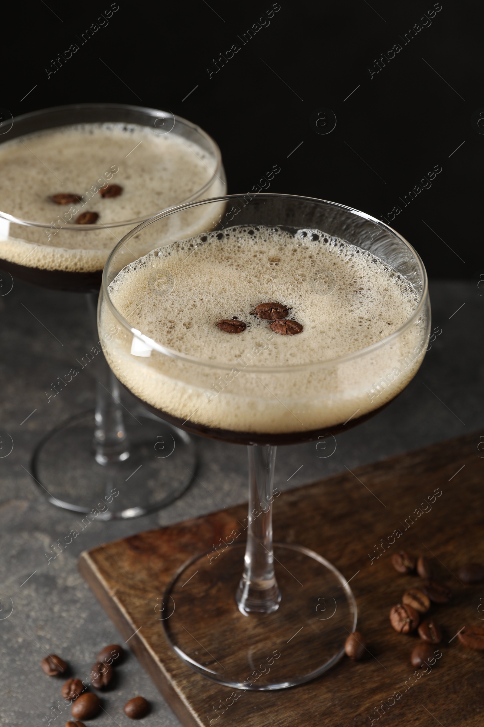 Photo of Glasses of delicious espresso martini and coffee beans on dark textured table, closeup