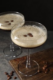 Glasses of delicious espresso martini and coffee beans on dark textured table, closeup