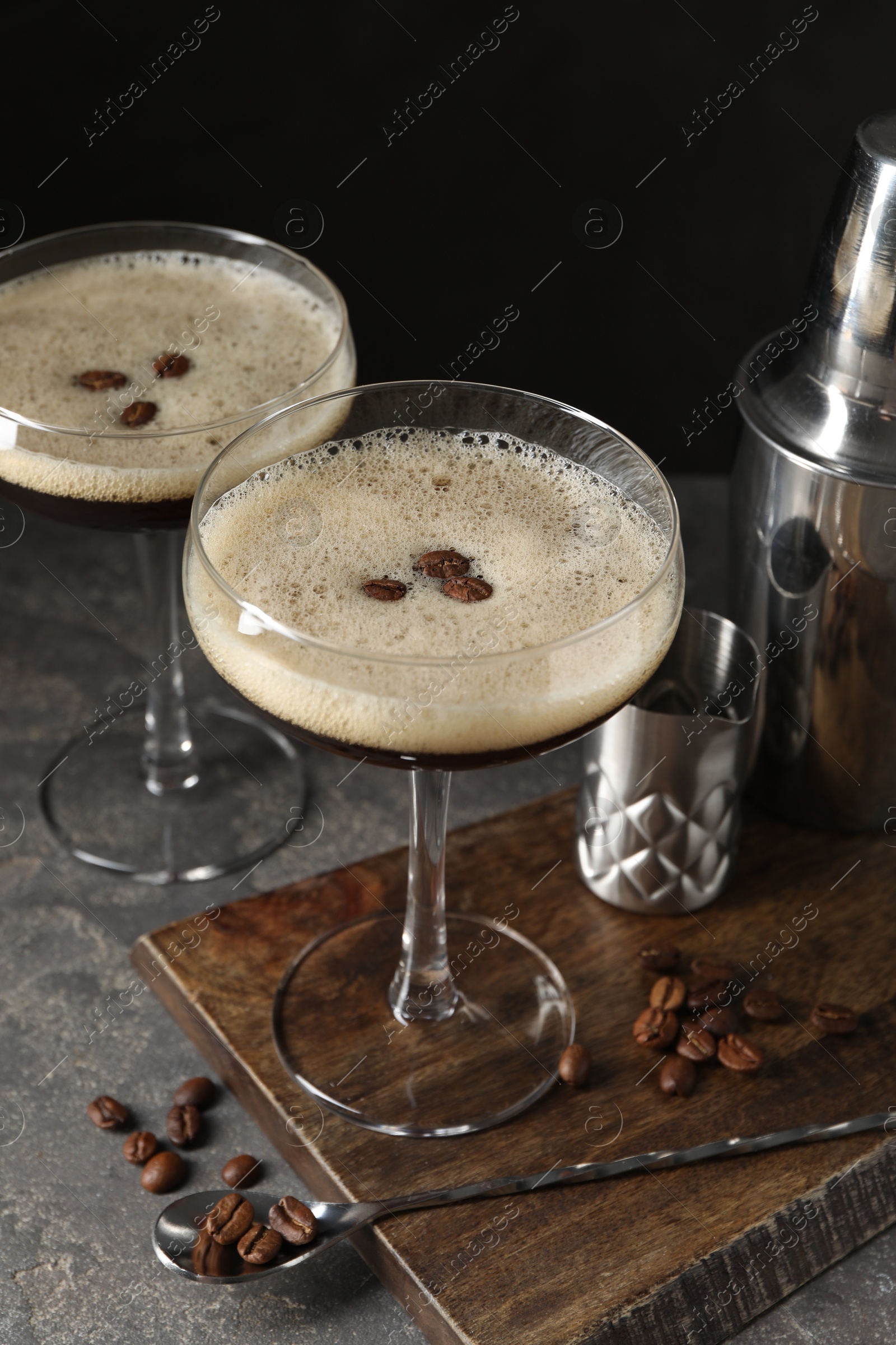 Photo of Glasses of delicious espresso martini and coffee beans on dark textured table, closeup