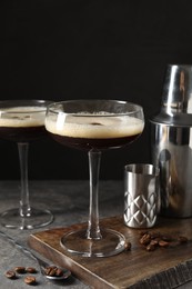 Glasses of delicious espresso martini and coffee beans on dark textured table, closeup