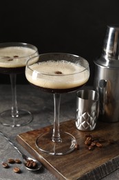 Photo of Glasses of delicious espresso martini and coffee beans on dark textured table, closeup