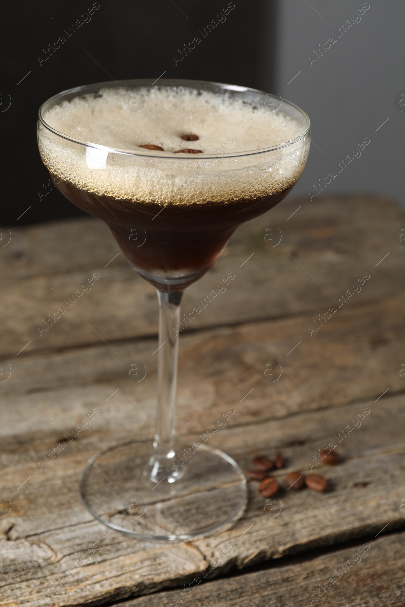 Photo of Glass of delicious espresso martini and coffee beans on wooden table, closeup