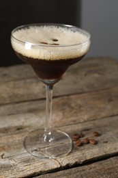 Glass of delicious espresso martini and coffee beans on wooden table, closeup