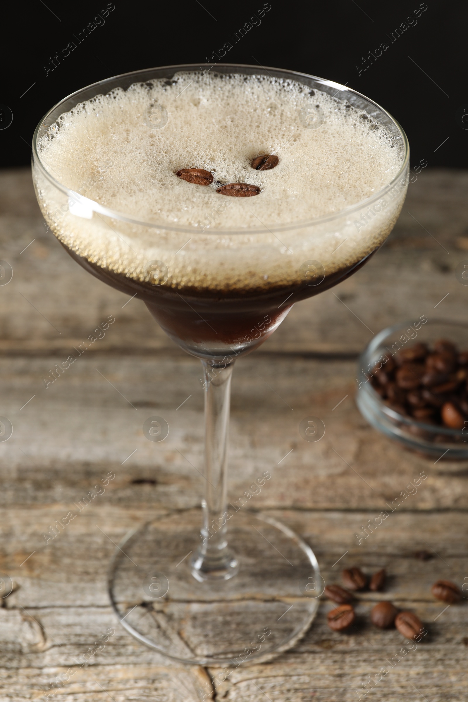 Photo of Glass of delicious espresso martini and coffee beans on wooden table, closeup