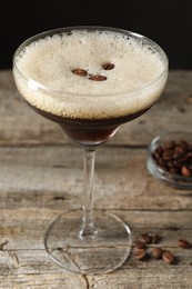 Glass of delicious espresso martini and coffee beans on wooden table, closeup