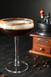 Photo of Glass of delicious espresso martini and coffee beans on dark textured table, closeup