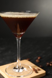 Photo of Glass with delicious espresso martini and coffee beans on dark table, closeup