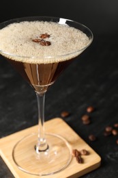 Glass of delicious espresso martini and coffee beans on dark textured table, closeup