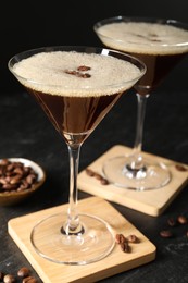 Photo of Glasses of delicious espresso martini and coffee beans on dark textured table, closeup