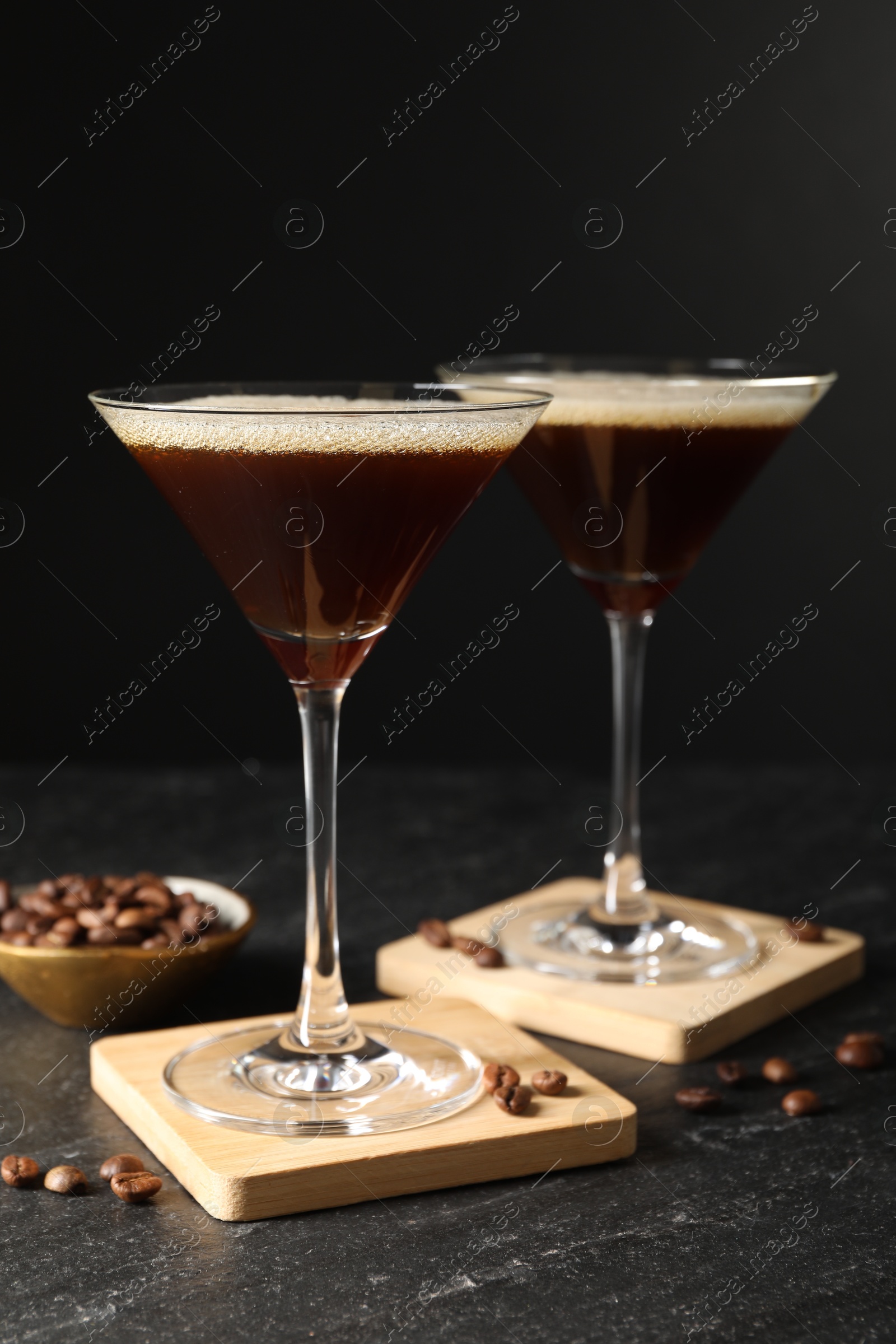 Photo of Glasses of delicious espresso martini and coffee beans on dark textured table