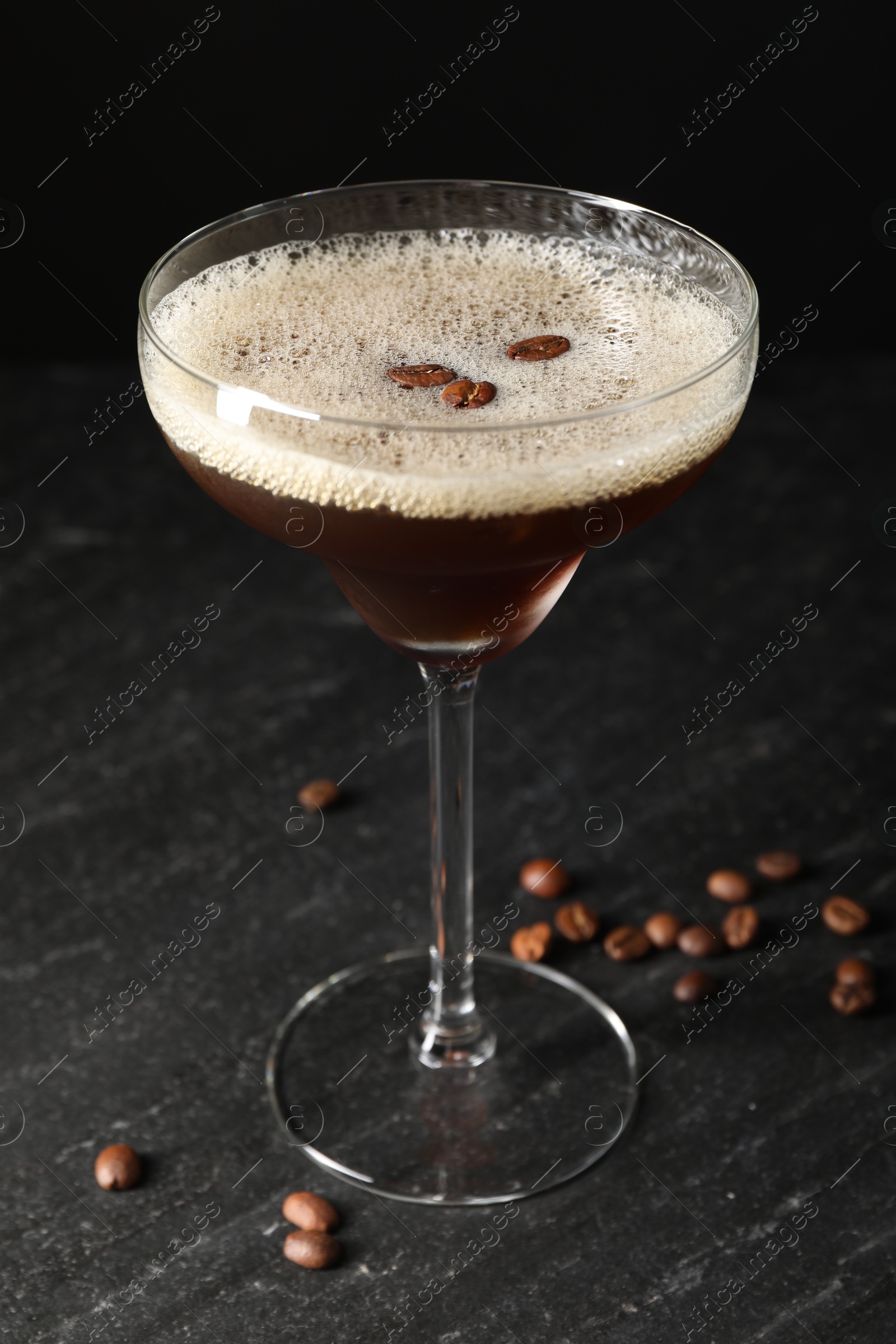 Photo of Glass of delicious espresso martini and coffee beans on dark textured table, closeup