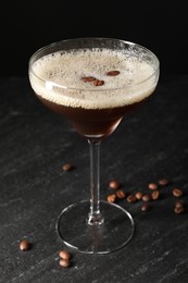 Glass of delicious espresso martini and coffee beans on dark textured table, closeup