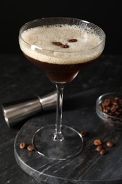 Photo of Glasses of delicious espresso martini, jigger and coffee beans on dark textured table, closeup