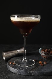 Photo of Glasses of delicious espresso martini, jigger and coffee beans on dark textured table, closeup