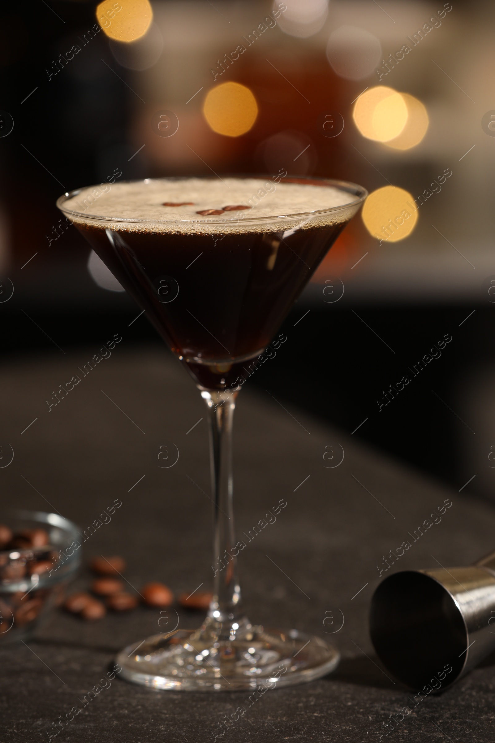 Photo of Delicious espresso martini in glass on table against blurred lights, closeup