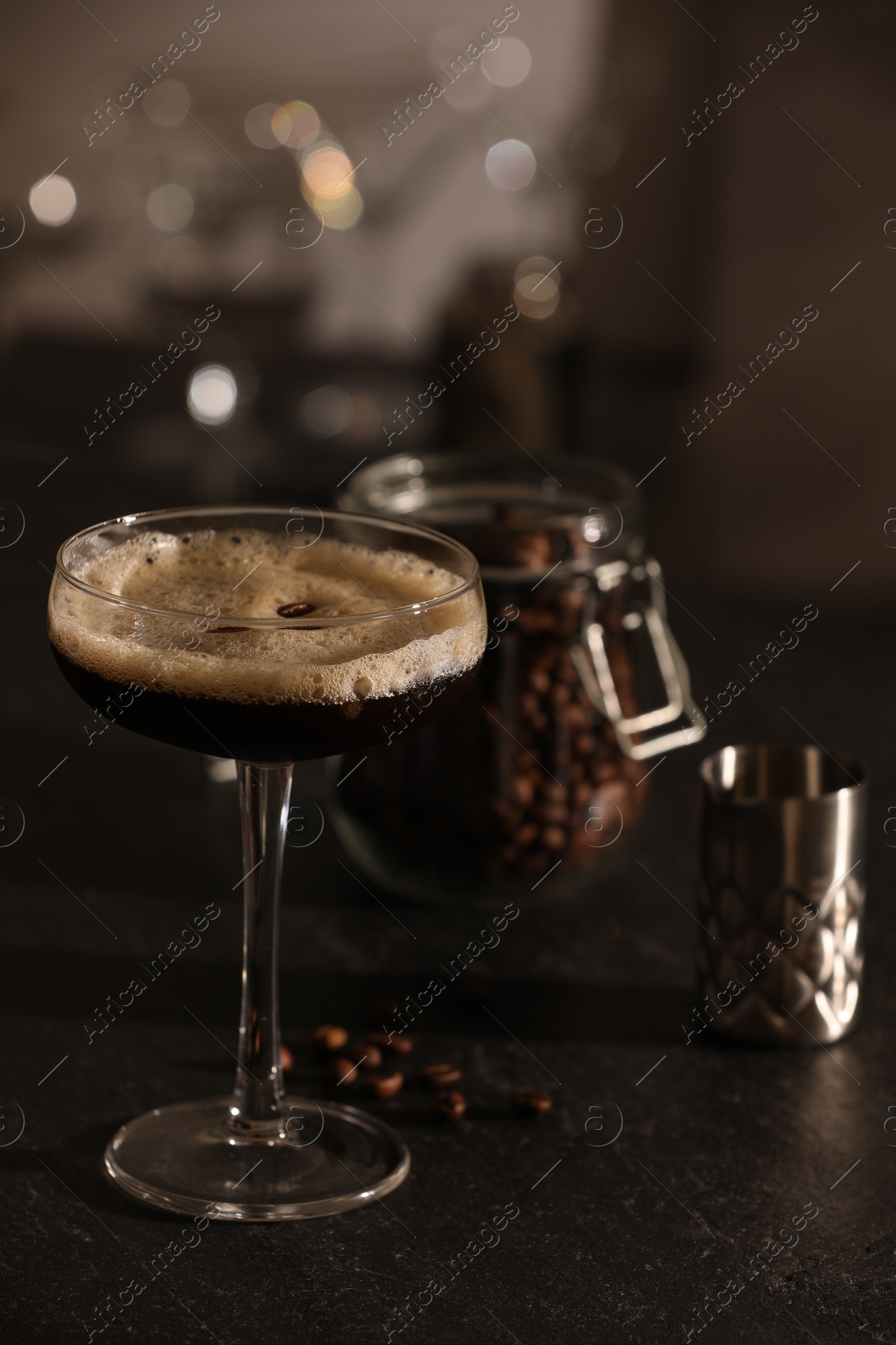 Photo of Glass with delicious espresso martini and coffee beans on dark table in bar