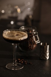 Glass with delicious espresso martini and coffee beans on dark table in bar