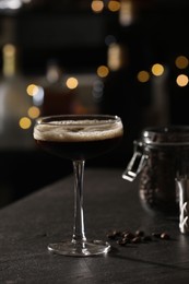 Photo of Glass with delicious espresso martini and coffee beans on dark table against blurred lights