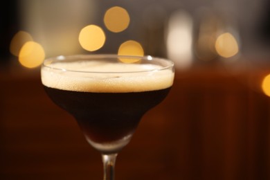 Delicious espresso martini in glass against blurred lights, closeup