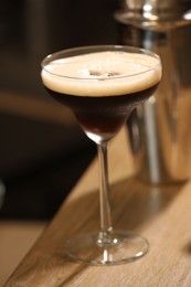 Photo of Glass with delicious espresso martini on wooden table in bar, closeup