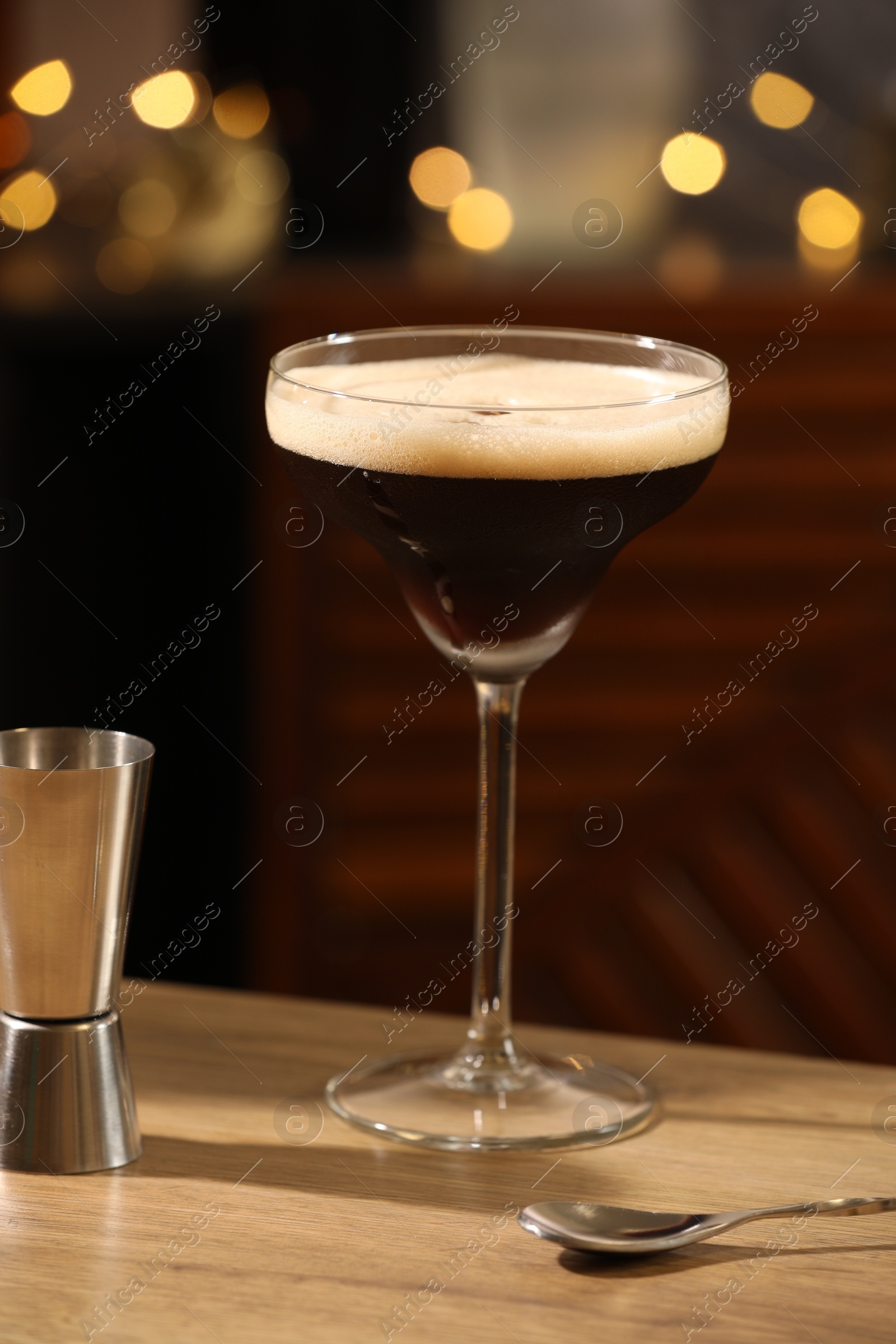 Photo of Glass with delicious espresso martini and jigger on wooden table in bar