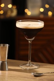 Glass with delicious espresso martini and jigger on wooden table in bar