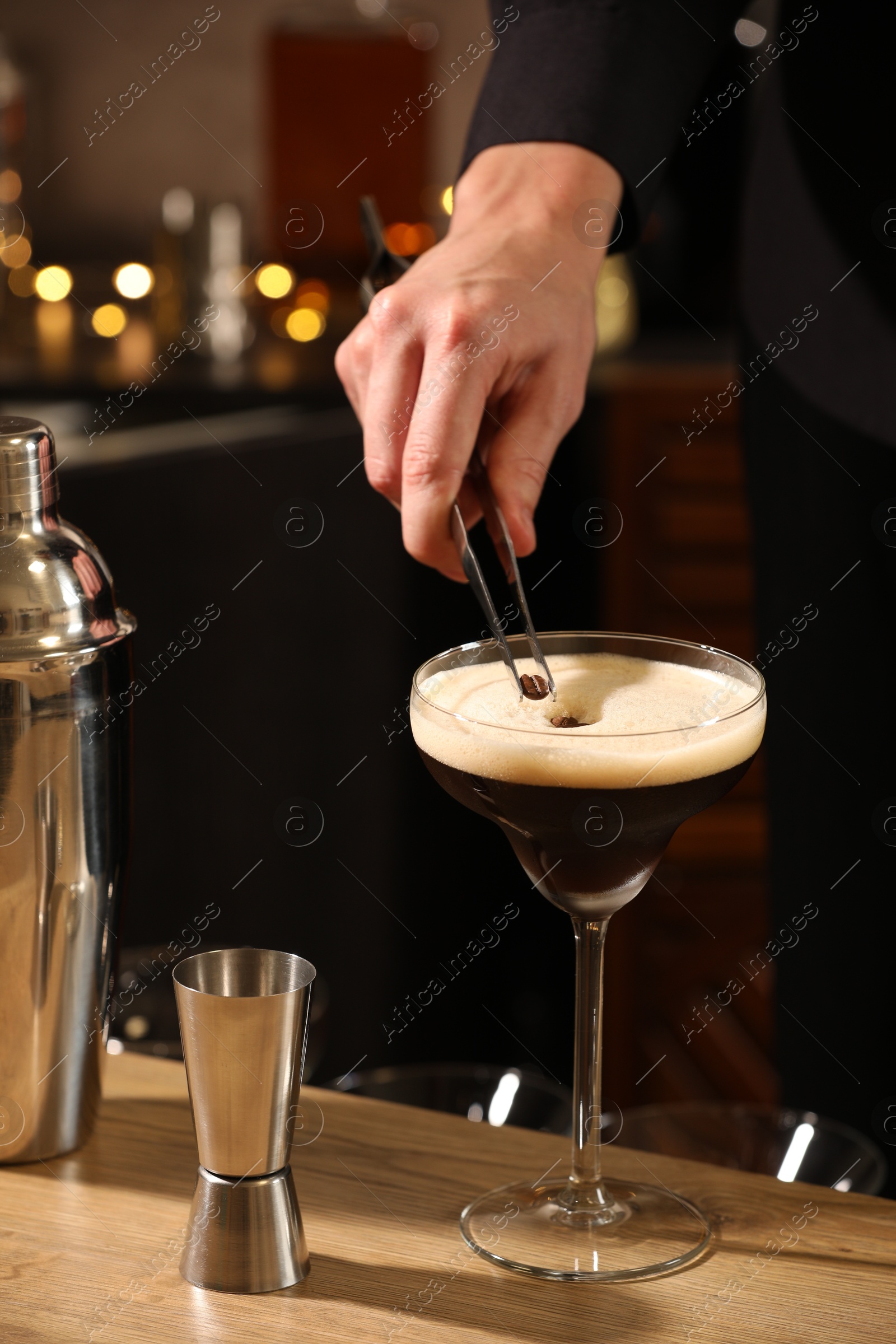 Photo of Bartender putting coffee bean into glass with delicious espresso martini at wooden table in bar, closeup