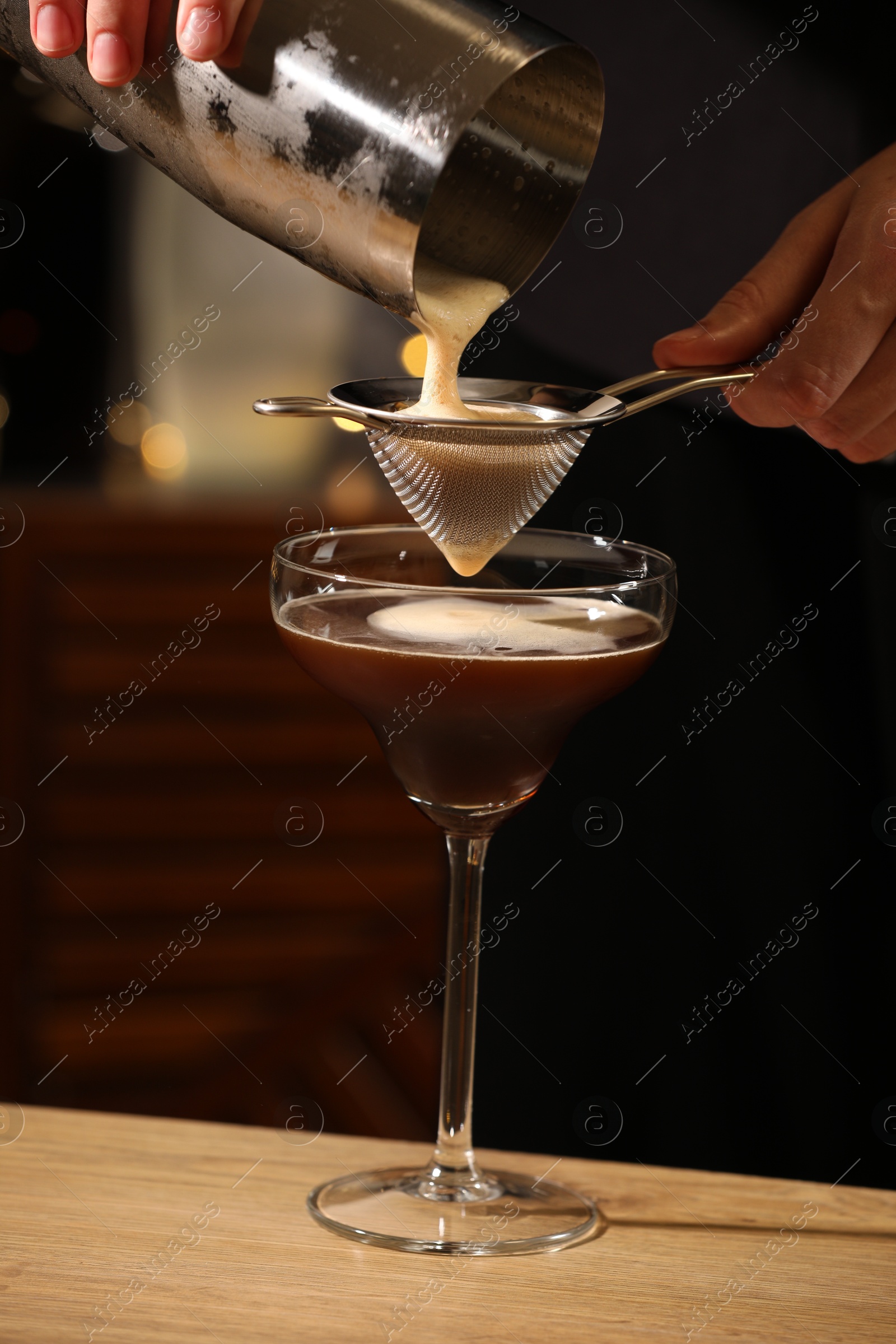 Photo of Bartender making delicious espresso martini at wooden table in bar, closeup