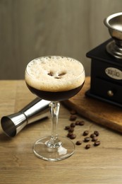 Photo of Delicious espresso martini in glass, coffee beans, manual grinder and jigger on wooden table