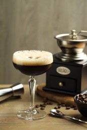 Photo of Delicious espresso martini in glass, coffee beans, manual grinder and jigger on wooden table