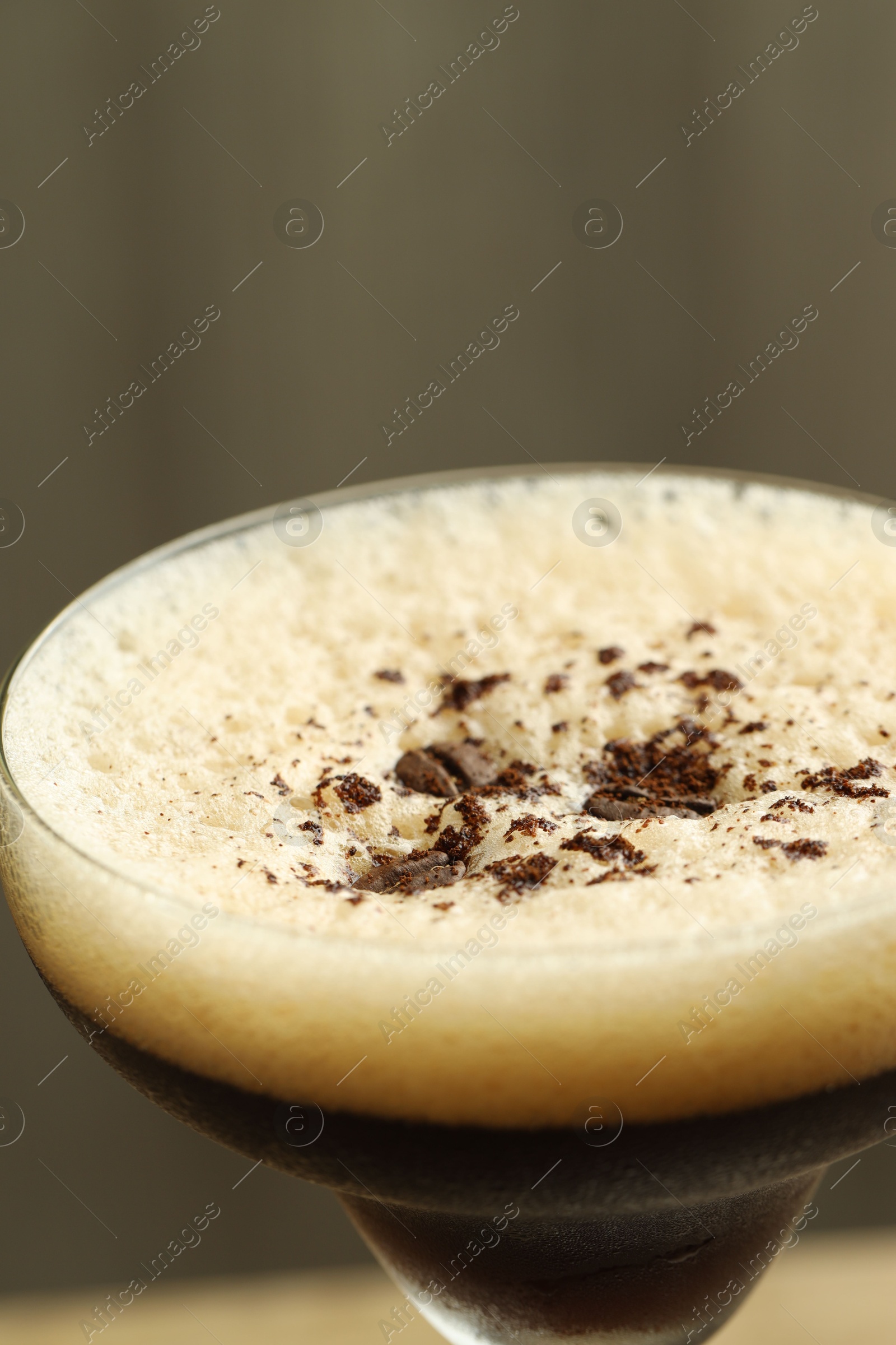 Photo of Delicious espresso martini with coffee beans in glass on blurred background, closeup