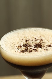 Photo of Delicious espresso martini with coffee beans in glass on blurred background, closeup