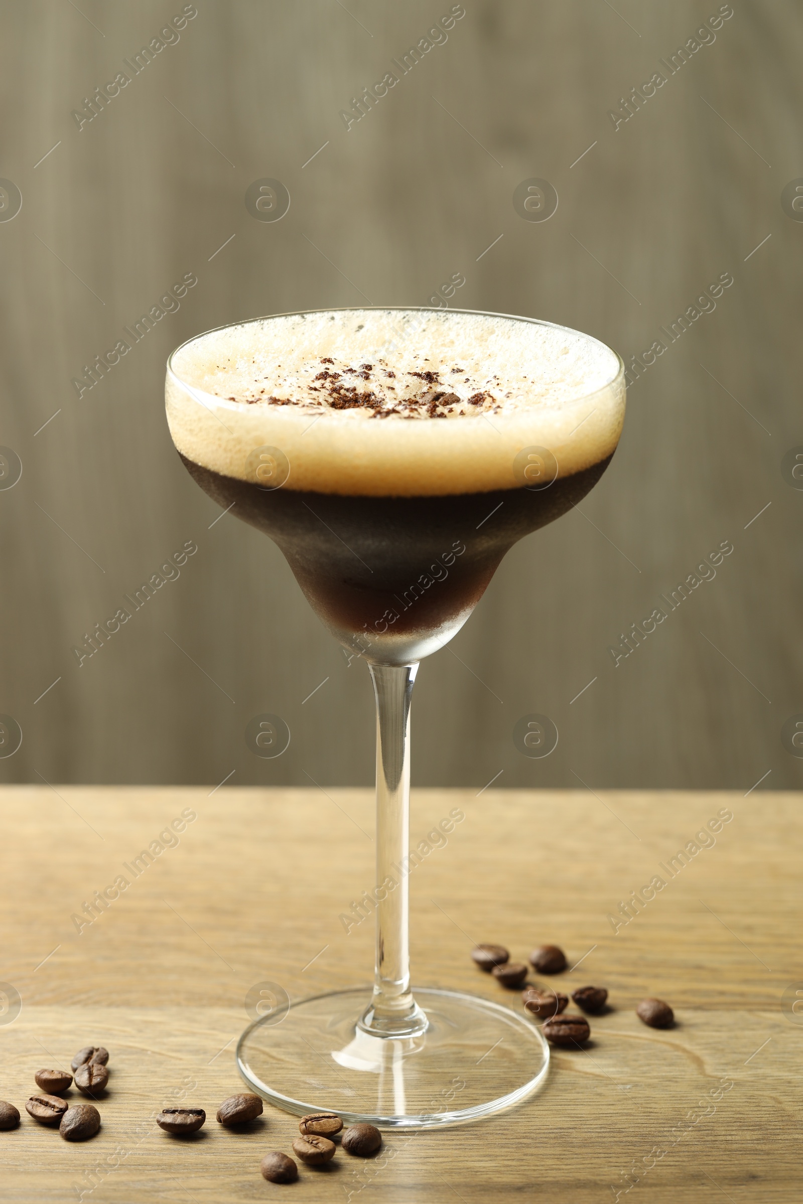 Photo of Delicious espresso martini in glass and coffee beans on wooden table